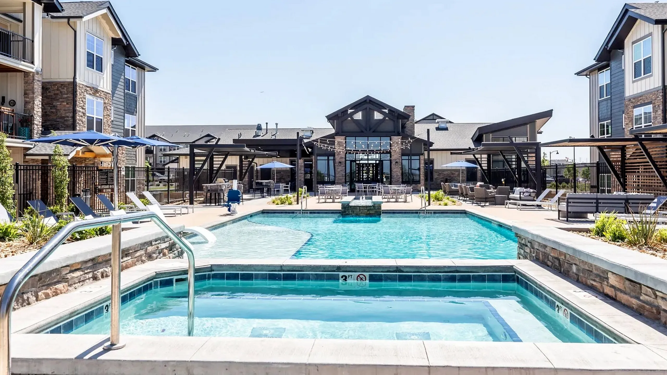 Luxurious apartment complex showcasing a sparkling swimming pool and relaxing hot tub surrounded by stylish seating areas, offering a perfect blend of comfort and elegance.