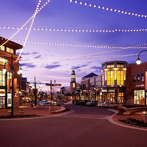 Vibrant evening view of a bustling shopping district with illuminated storefronts, charming streetlights, and a picturesque twilight sky.