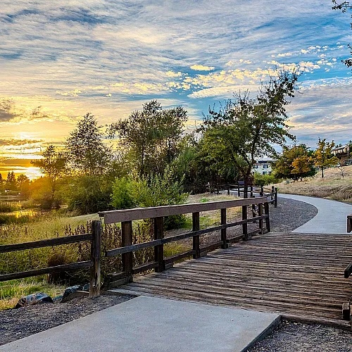 Scenic walkway through a serene natural landscape with vibrant sunset skies, perfect for a tranquil evening stroll.