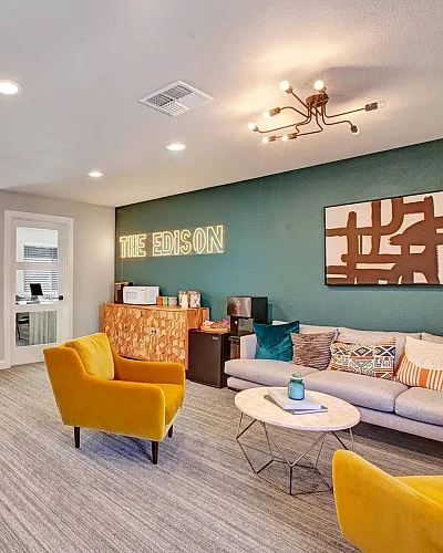 Modern lounge area at The Edison with vibrant decor, featuring stylish yellow chairs, a cozy sofa with decorative pillows, and a contemporary lighting fixture.