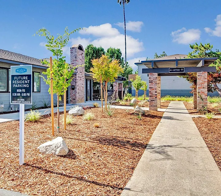 Charming community area with modern brick buildings, lush landscaping, and inviting pathways under a clear blue sky.