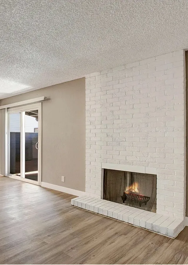 Bright and inviting living room with elegant wooden flooring, a cozy white brick fireplace, and sliding glass doors leading to a serene outdoor space.