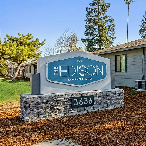 Inviting entrance to The Edison Apartment Homes surrounded by lush greenery and serene landscaping.