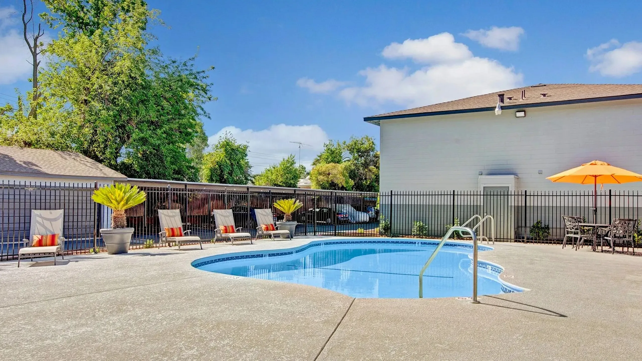 Inviting outdoor pool area with stylish lounge chairs, vibrant umbrellas, and lush greenery under a bright blue sky.