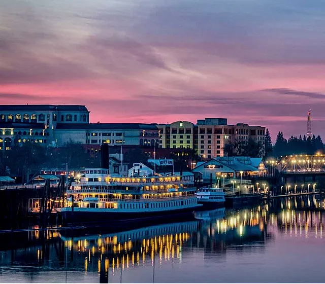 Captivating evening view of The Railyards with a beautifully illuminated bridge and riverfront, highlighted by a breathtaking purple sunset skyline.