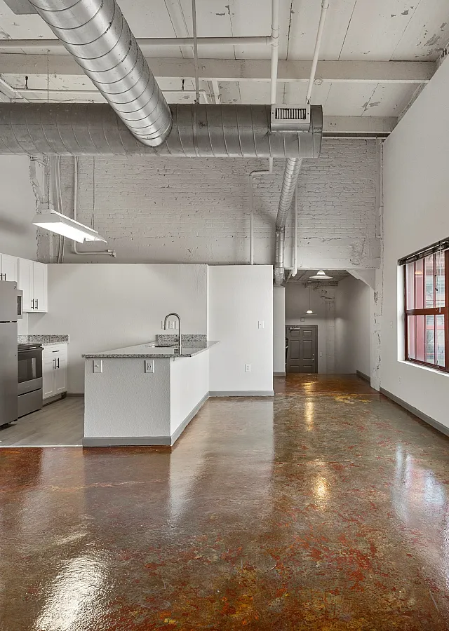 Industrial-style apartment featuring high ceilings, exposed ductwork, and large windows offering natural light in an open-concept kitchen and living area.