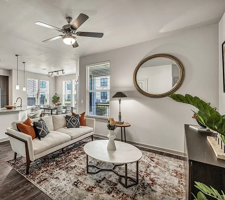 Modern open-concept living room and kitchen with stylish decor, featuring a cozy sofa, sleek ceiling fan, and bright natural lighting.