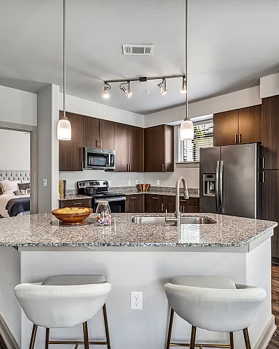 Modern kitchen with sleek granite countertops, stainless steel appliances, and elegant wood cabinetry, featuring a cozy breakfast bar and stylish pendant lighting.