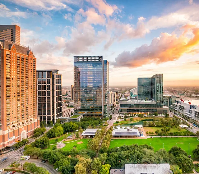 Vibrant cityscape view featuring modern skyscrapers, lush green park, and a stunning sunset sky, offering a perfect urban living experience.