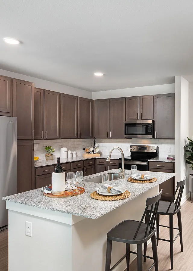 Sleek modern kitchen with dark wood cabinets, stainless steel appliances, and a stylish granite island with seating, accented by contemporary art and a lush potted plant.
