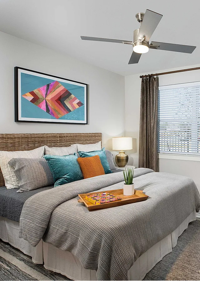 Cozy and elegant bedroom featuring a plush bed with colorful pillows, stylish artwork, and natural lighting from a large window.