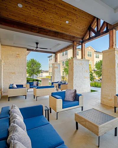 Inviting covered patio area with stylish blue seating and modern stone pillars, overlooking a pristine pool and beautifully landscaped gardens.