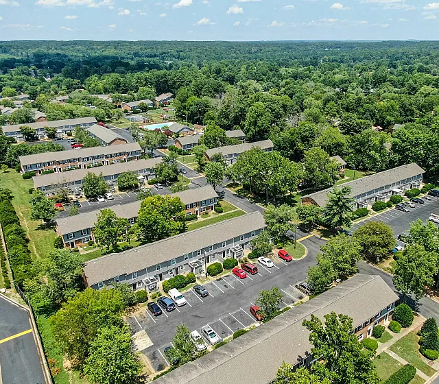 Aerial view of a lush, green suburban apartment community with neatly arranged buildings, spacious parking, and scenic natural surroundings.