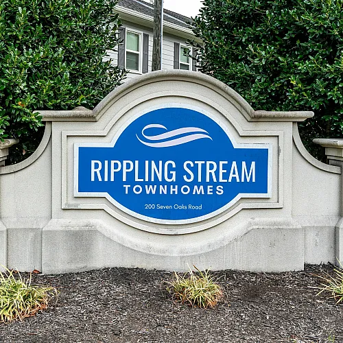 Inviting entrance sign for Rippling Stream Townhomes, showcasing elegant design and lush greenery at 200 Seven Oaks Road.