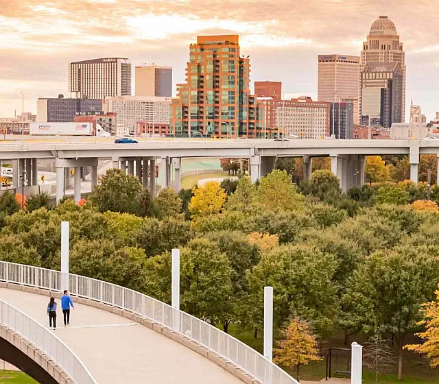 Vibrant cityscape view with lush greenery and a scenic walking path leading towards the skyline at sunset.