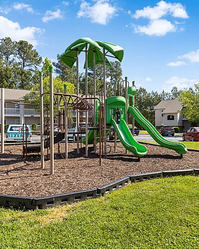 Inviting residential playground with vibrant green slides and modern equipment, set against a backdrop of charming townhouses and lush greenery.