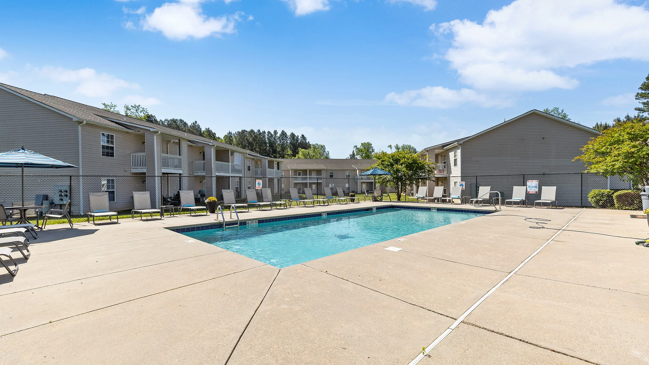 Inviting apartment community with a sparkling pool, sun loungers, and a sunny courtyard, perfect for relaxation and leisure.