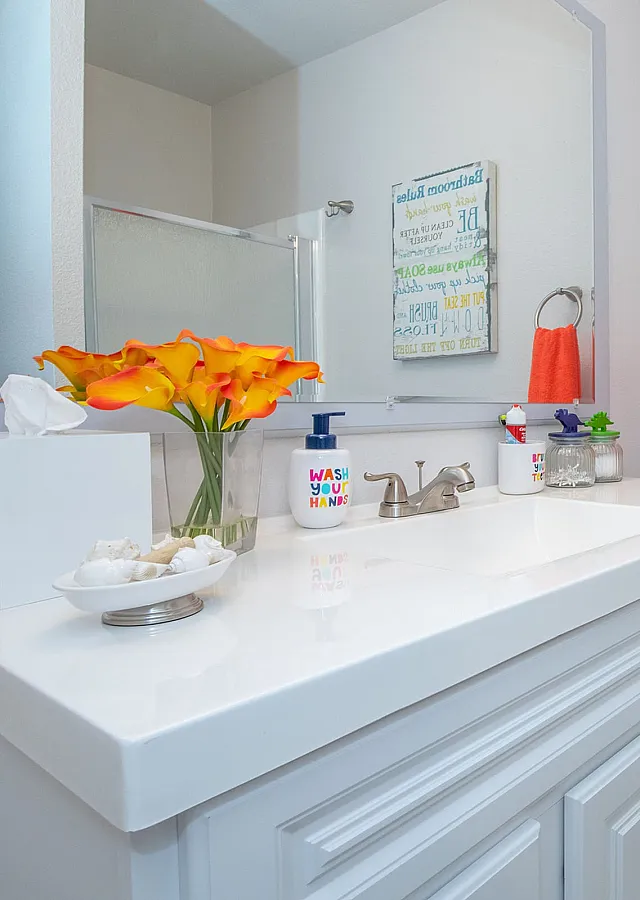 Bright and modern bathroom with white cabinetry, vibrant orange towels, and cheerful floral accents creating a welcoming atmosphere.