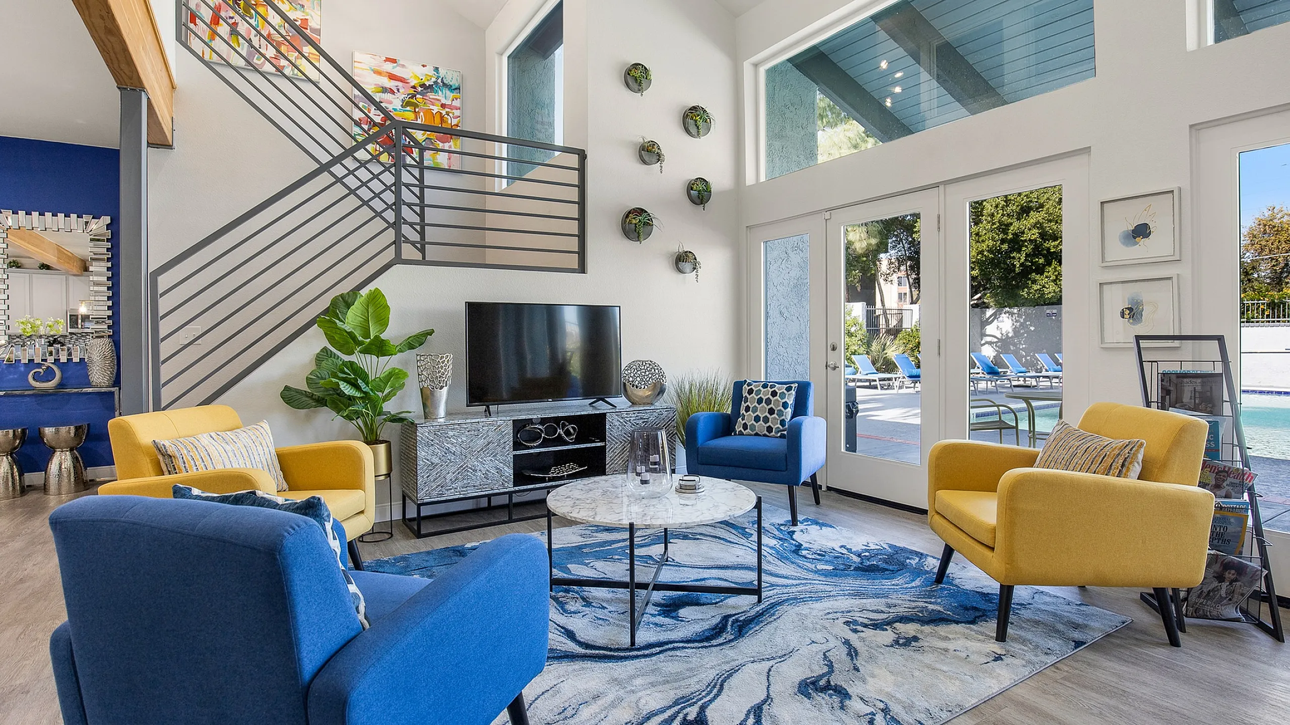 Vibrant, sunlit living room with modern design, featuring colorful armchairs, sleek decor, and a view of the pool area through large glass doors.