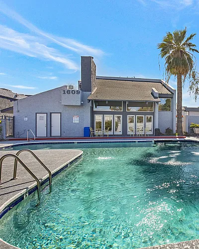Inviting apartment community featuring a sparkling swimming pool, lounge chairs, and modern clubhouse under a clear blue sky.