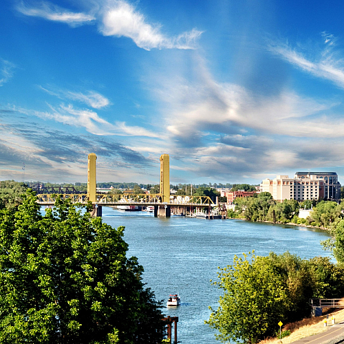 Scenic riverside view of a vibrant cityscape featuring a historic bridge, lush greenery, and captivating blue skies.