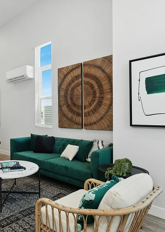 Modern living area with high ceilings, stylish green sofa, chic kitchen with dark cabinetry, and elegant artwork accents.