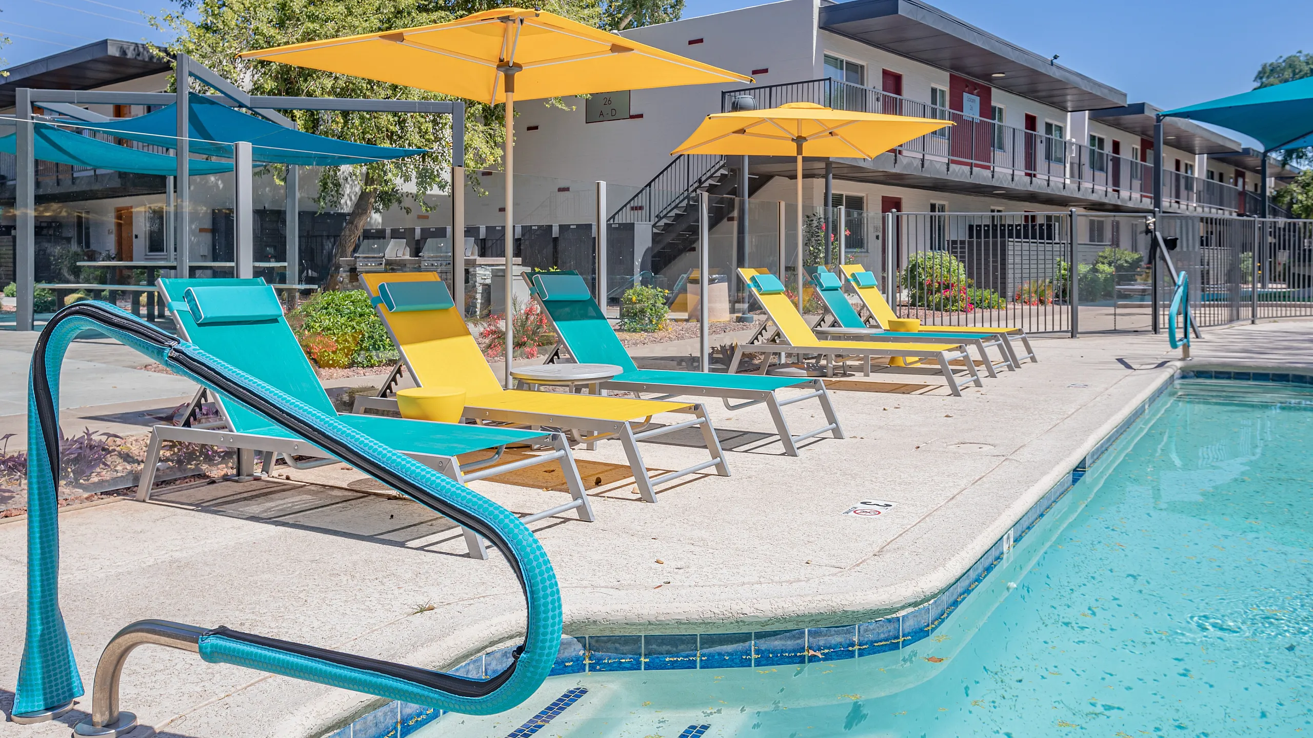 Inviting apartment complex with vibrant pool area, modern loungers, and sun umbrellas set against a sunny backdrop.