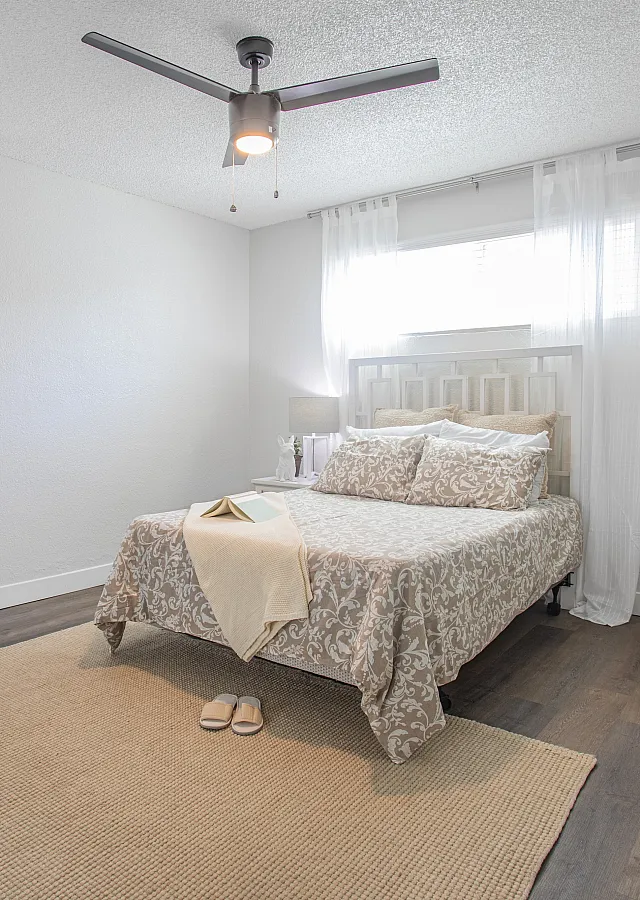 Bright and inviting bedroom with elegant decor, featuring a cozy bed, modern ceiling fan, and chic workspace under natural light.