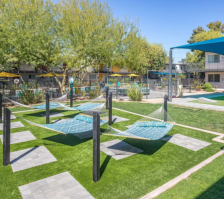 Inviting apartment complex outdoor area with cozy hammocks, vibrant green lawn, and shaded seating, perfect for relaxation and community gatherings.