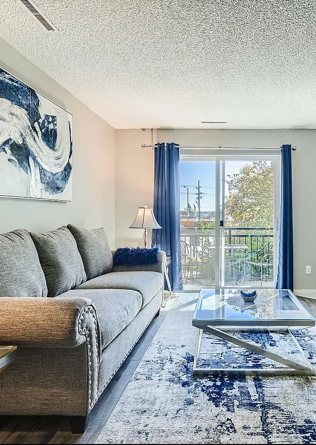 Bright and elegant living room with a trendy gray sofa, modern art decor, and a cozy fireplace, featuring large windows and stylish flooring.