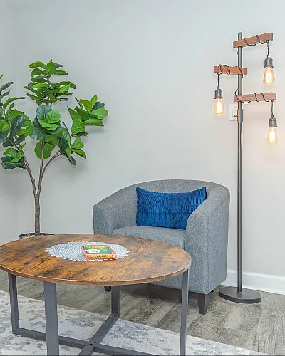 Chic and inviting living area with cozy gray armchairs, a stylish wooden coffee table, vibrant indoor plant, and modern lighting.