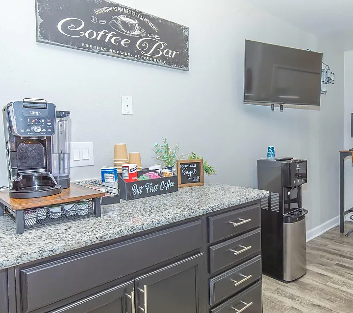 Inviting apartment space featuring a chic coffee bar with a Ninja coffee maker, sleek granite countertops, and a cozy workspace with stylish bar stools.