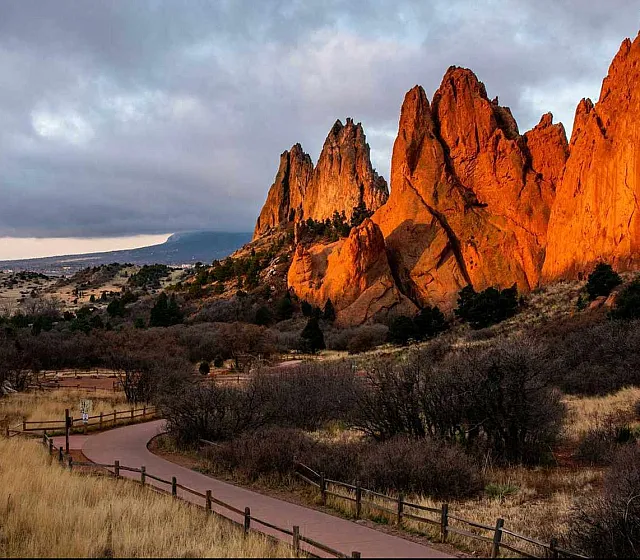 Breathtaking landscape showcasing majestic red rock formations glowing in sunset light with a scenic trail leading through a picturesque valley.