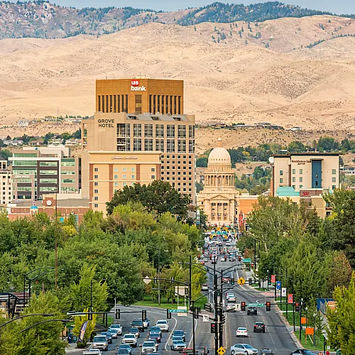Vibrant cityscape featuring bustling streets lined with lush trees, modern buildings, and scenic mountain backdrop.