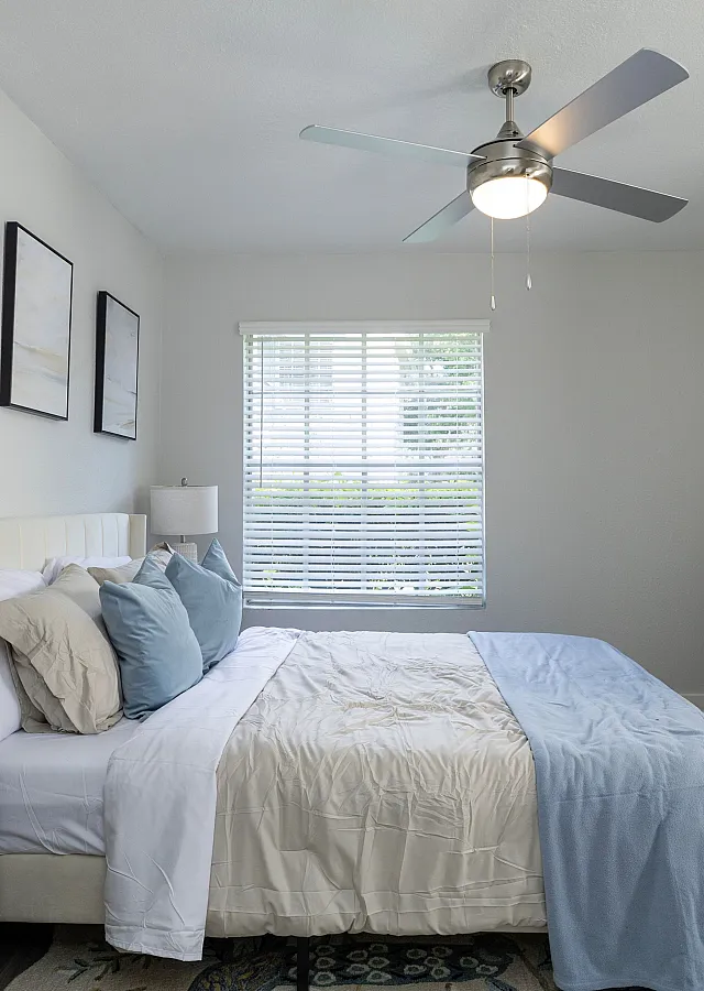 Bright and inviting bedroom with elegant decor, a cozy bed with soft pillows, stylish ceiling fan, and natural light filtering through a window, creating a serene atmosphere.