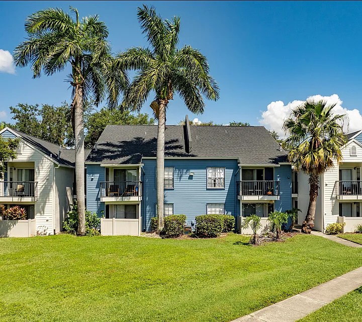 Charming apartment complex with vibrant blue and white facade, surrounded by lush greenery and majestic palm trees, offering a serene living environment.
