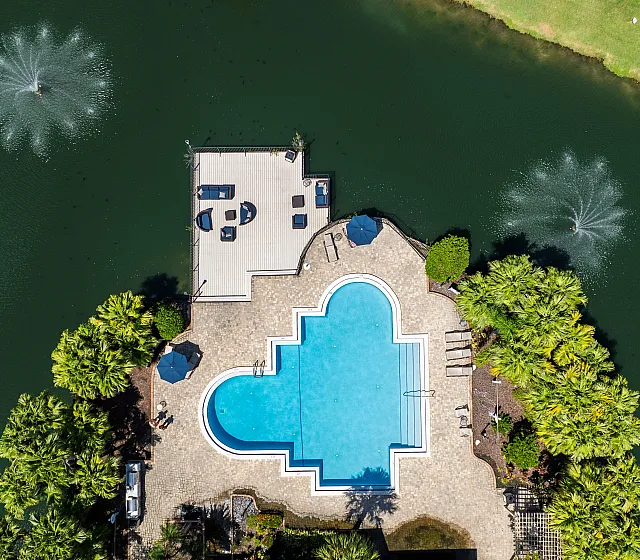 Aerial view of a luxurious pool shaped like a heart, surrounded by lush greenery and overlooking a serene lake with elegant fountains.