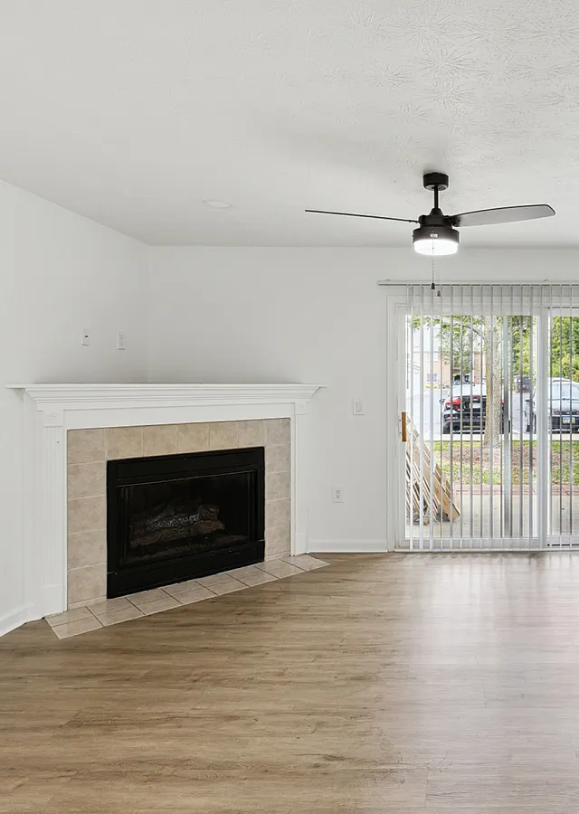 Bright and spacious living room with elegant hardwood floors, a cozy fireplace, and large sliding glass doors opening to a lush outdoor view.