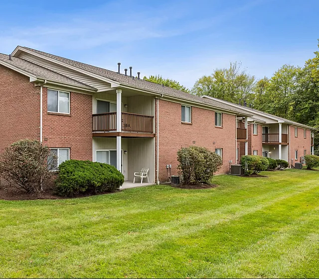 Charming brick apartment complex with lush green surroundings and spacious balconies, perfect for serene living.