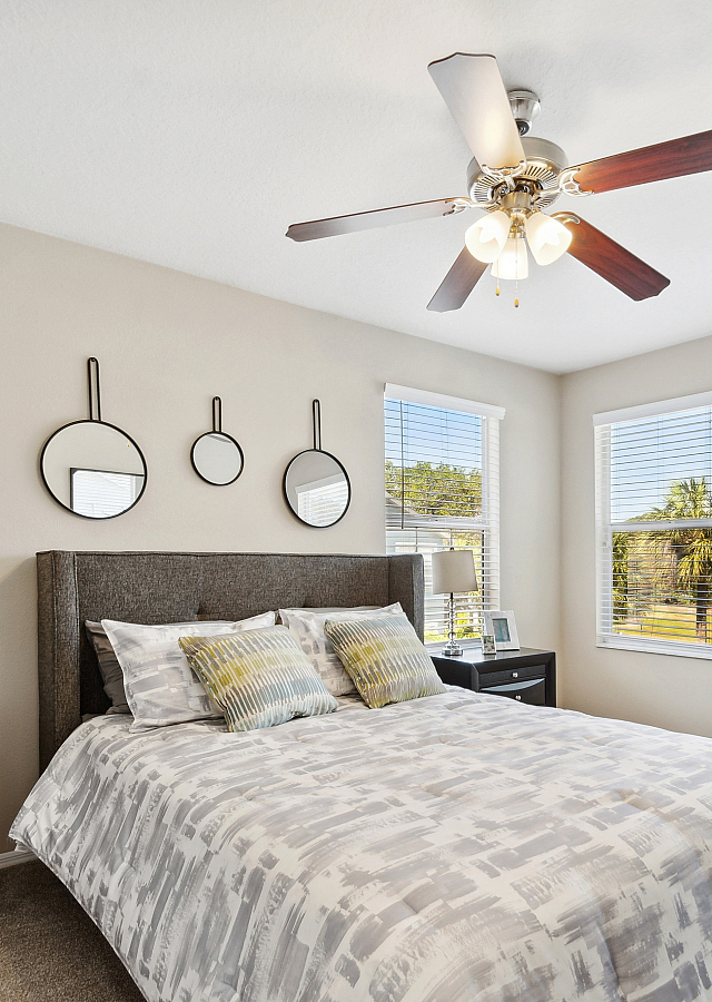 Bright and inviting bedroom with stylish decor, featuring large windows, a chic ceiling fan, and modern furniture providing a tranquil space.