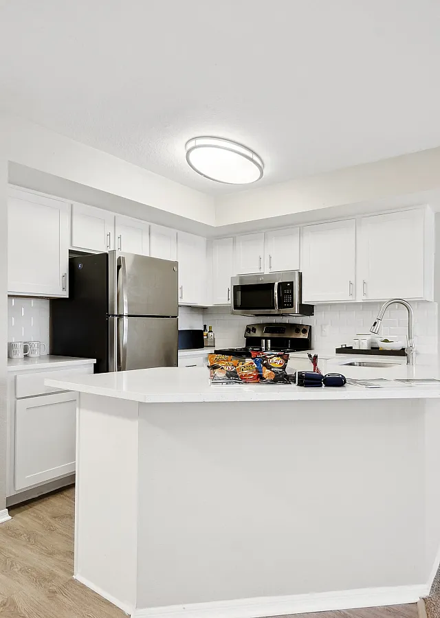 Bright, modern kitchen with sleek white cabinetry, stainless steel appliances, and an inviting open layout leading to a cozy bedroom.