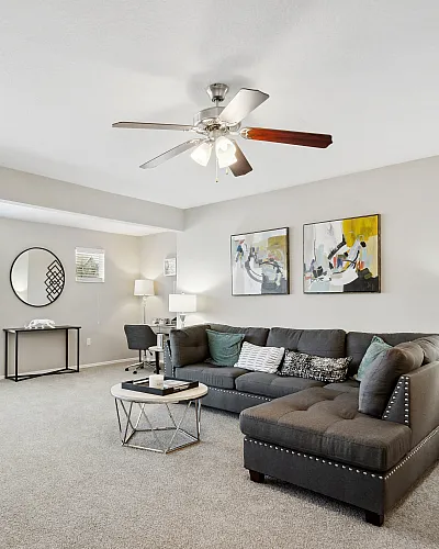 Bright and welcoming living room with modern gray sectional sofa, contemporary artwork, and large windows offering abundant natural light.