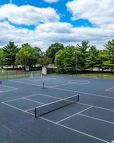Expansive sports court featuring tennis and basketball setups surrounded by lush greenery and clear skies.