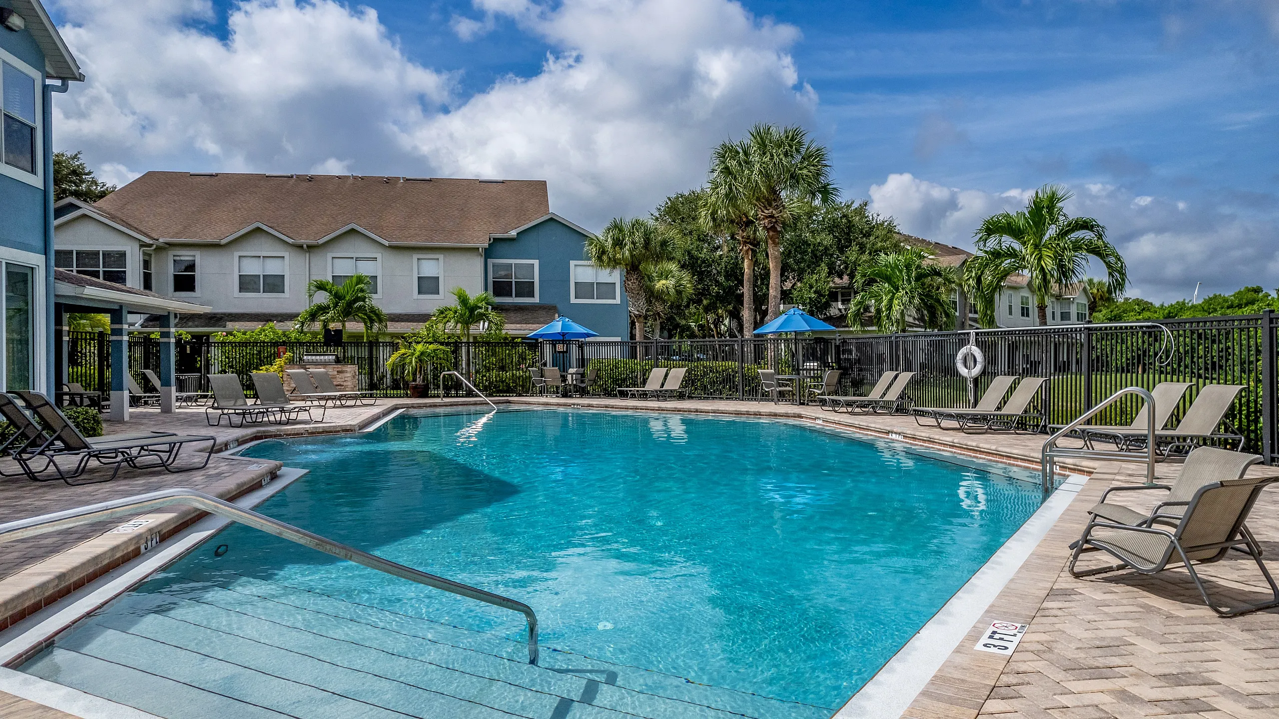 Inviting outdoor pool area with sun loungers surrounded by lush palm trees, perfect for relaxation and leisure in a serene residential setting.