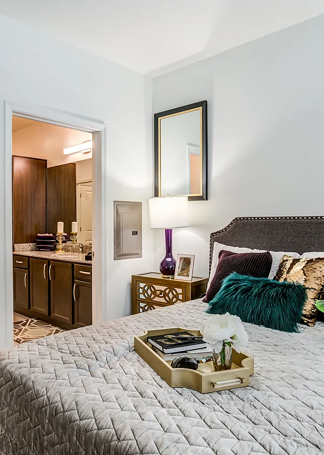 Inviting bedroom with elegant decor, showcasing a cozy bed adorned with plush pillows, a stylish nightstand, and an attached walk-in closet leading to a modern bathroom.