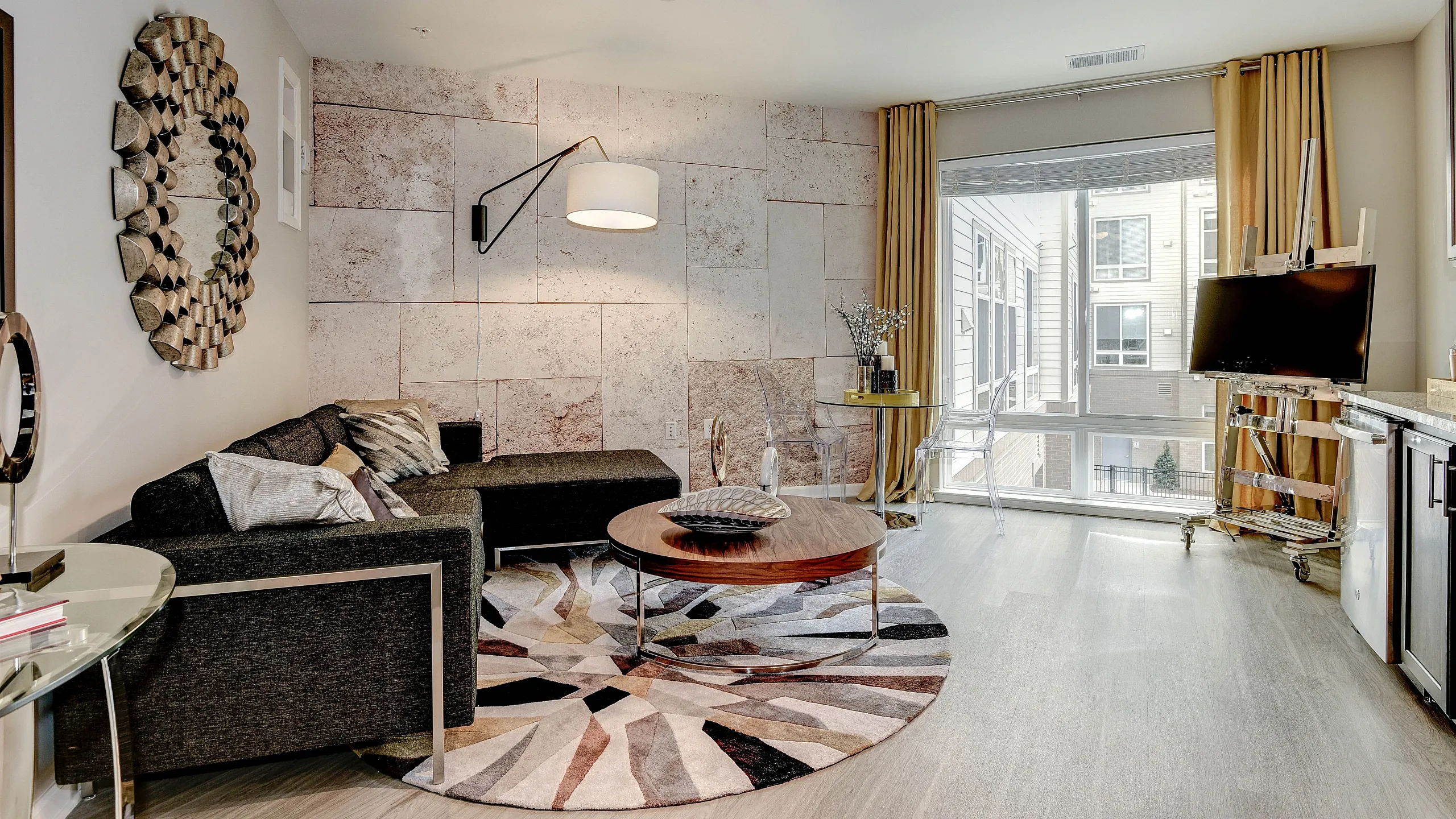 Elegant modern living room with sleek furniture, artistic wall mirror, and large windows offering abundant natural light.