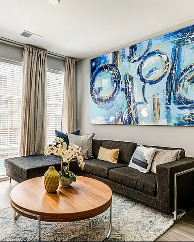Chic living room with a contemporary gray sofa, large abstract art, and bright windows enhancing warmth and style.