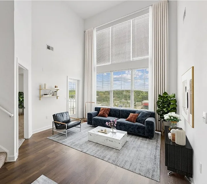 Bright and airy living room with high ceilings, large windows, and modern furnishings including a plush navy sofa and sleek accents.