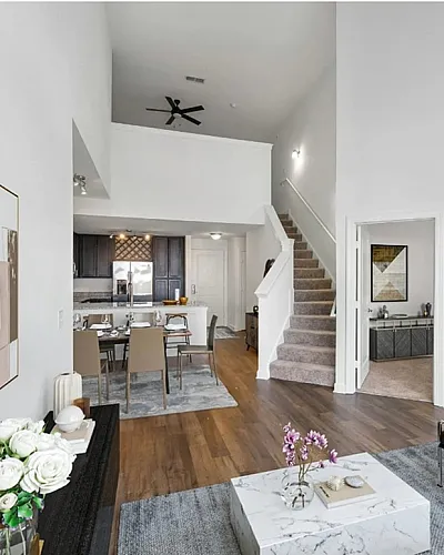 Chic open-concept living area with modern decor, featuring a cozy seating arrangement, elegant dining space, and stylish kitchen. Inviting staircase leading to second floor; perfect for contemporary living.