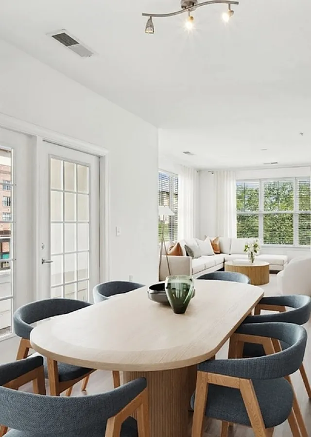 Bright and modern open-concept living area featuring a cozy dining space with stylish chairs, a sleek kitchen with a granite countertop, and a light-filled lounge with a large sectional sofa.